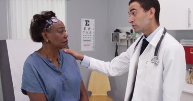 Genç Latin doktor yaşlı Afrikalı kadınla sağlık sorunlarını tartışıyor. Tıp doktoru hastaların omzunda dinlenirken sempati gösteriyor.