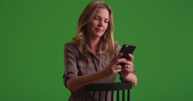 Orta yaşlı beyaz kadın yeşil ekranda akıllı telefondan mesajlaşıyor. Anahtar ya da birleşik olmak üzere yeşil ekranda.