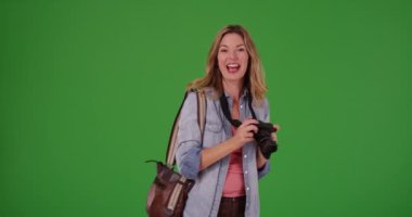 Orta yaşlı beyaz kadın fotoğraf çekiyor ve yeşil ekranda kamerayla konuşuyor. Anahtar ya da birleşik olmak üzere yeşil ekranda.