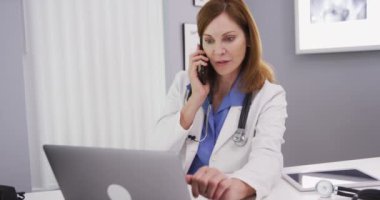 Hasta ile telefonda konuşurken dizüstü bilgisayar kullanan sevimli kadın doktorun portresi. Akıllı telefon cihazıyla konuşurken dizüstü bilgisayarda yazan kadın doktoru kapat