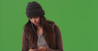 Beyaz perdenin önünde akıllı telefonuyla müzik dinleyen sevimli beyaz kız. Yeşil ekranda müzik dinlemek için kulaklık takan çekici genç bir kadın. 4k