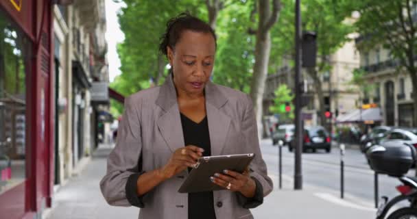 黑人女商人在城市街道上使用数字平板电脑 成熟的非洲裔美国女人在巴黎街上使用无线触摸屏电脑 — 图库视频影像