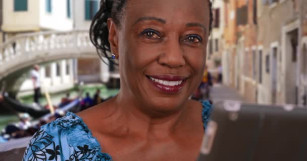 大運河のデジタルタブレットを使用して高齢者の黒人女性の肖像画 引退したアフリカ系アメリカ人女性はヴェネツィアで肖像画のポーズをとる — ストック動画