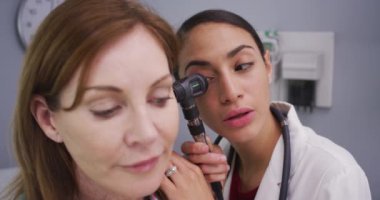 Kulağı genç Latin doktor tarafından otoskopla muayene edilen son sınıf bayan hasta. Genç doktorun tıbbi aletle hastaların kulaklarını kontrol etmesine yakın durun.