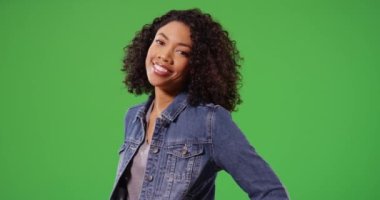 Kot ceketli gülen siyahi kadının portresi yeşil ekrana komik bir şekilde poz veriyor. Afro-Amerikan Milenyum kızı gülümseyen ve yeşil ekranda çizim ya da kompozitasyon için poz veren tarzını kapatın. 4k