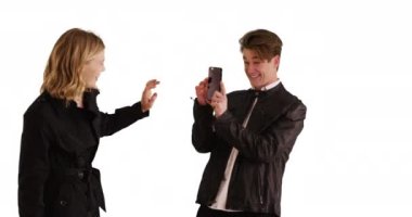 Erkek, cep telefonlu utangaç kız arkadaşının beyaz arka planda fotokopisini çekiyor. Mutlu genç çift stüdyoda fotokopi odasıyla kucaklaşıyor. 4k