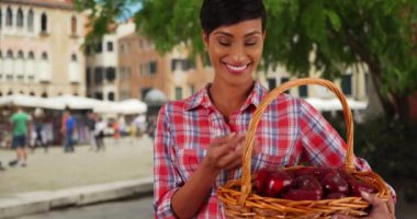 Neşeli gülümseyen siyah kadın bahçıvan sepet dolusu taze elmayla poz veriyor. Venedik, İtalya 'da güzel bir Afro-Amerikalı kadının gülümseyerek eline elma attığı portre. 4k