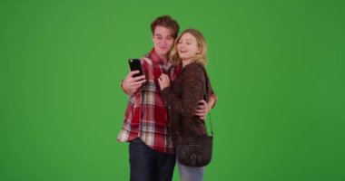 Genç milenyum çifti yeşil ekranda cep telefonuyla selfie çekiyor. Anahtar ya da birleşik olmak üzere yeşil üzerine.