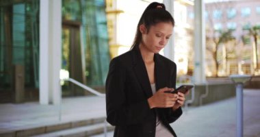 Şehir merkezindeki güzel iş kadını akıllı telefondan mesaj atıyor. 4G mobil cihaz kullanarak spor ceket giymekte başarılı bir kadın. 4k