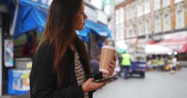 Bombacı ceketli hippi kız Londra 'da cep telefonuyla mesajlaşıyor. Brixton Caddesi 'ndeki marketin yakınındaki akıllı telefonunda kahve olan sıradan esmer bir kadın. 4k