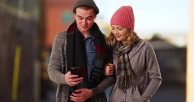Genç bir çift ya da kışlık giysiler içinde dışarıda yürüyüş yapan ve yol tarifi için cep telefonunu kullanan arkadaşlar. Erkek ve dişi kol kola girmiş, konuşuyor ve gülümsüyor. 4k