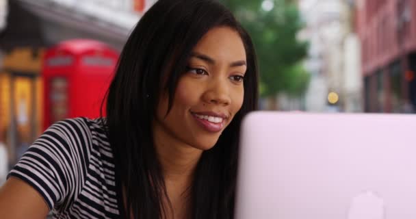 ラップトップで働いているロンドンの通りで魅力的な黒人女性のクローズアップ ビジネスの女性が屋外でコンピュータ上でインターネットを使用して座っている — ストック動画
