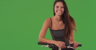 Bisiklette oturan ve yeşil ekranda poz veren çekici genç kadın portresi. Yeşil ekran duvarın önünde bisiklete binmiş gülümseyen güzel beyaz kızın yakın çekimi. 4k