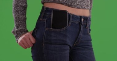 Mavi kotlu, elleri arka cebinde, ön cebinde akıllı telefonu yeşil ekranda olan bin yıllık bir kadın. Cep telefonlu bir kızın orta bölümünü kapatın. Tuşlama veya birleştirme için yeşil üzerine 4K