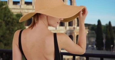 Roma 'da güneş şapkası takan güzel beyaz bir kızın arka manzarası. Yazın Kolezyum 'un yanında şık bir kadın turist. 4k