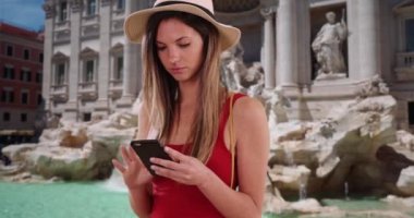 Kırmızı bluzlu şık bir kadın telefonla Roma, İtalya 'daki ünlü fıskiyeye bakıyor. 20 'li yaşlarda beyaz bir kız Trevi Fountain' da akıllı telefondan mesaj atıyor. 4k