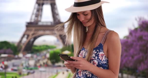 フランスの電話で花のルーマーとフェドーラのテキストメッセージの幸せな女性 エッフェル塔によるパリの携帯電話での20代のテキストメッセージの千年の少女 — ストック動画