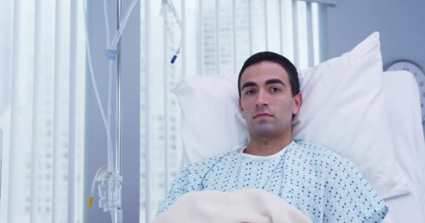 病院のベッドに横になってカメラを見ている大人の男性ラテン系患者の肖像画 手術を受けた後の回復における魅力的なパニック患者の近いビュー — ストック動画