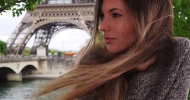 Eiffel Kulesi 'nin orada rüzgarda esen uzun kahverengi saçlı güzel bir kadın. Düşünceli ve ciddi bir genç bayan Paris, Fransa 'da bir tarafa bakıyor. 4k