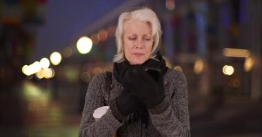 Üst düzey bir kadın eldivenini dişleriyle çıkarıp gece açık havada akıllı telefondan mesaj atıyor. Şallı ve süveterli yaşlı beyaz kadın akşam birini beklerken akıllı telefon kullanıyor. 4k
