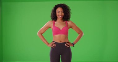 Yeşil ekranda elleri kalçalarında duran kendine güvenen sağlıklı siyah bir atlet. Yeşil ekranda spor kıyafetleri içinde gülümseyen Afrikalı Amerikalı genç bir kadın. 4k