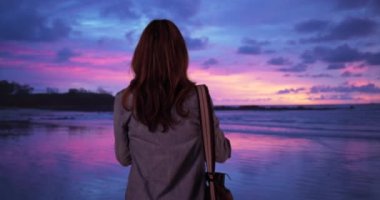 Kadın gün batımında okyanusun fotoğrafını çekiyor. Sahilde duran ve akşamları sakin kıyı şeridinin fotoğrafını çeken kadın turist. 4k