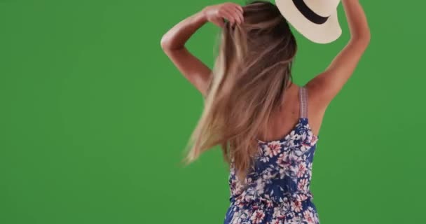 若い女性の背面ビューは帽子を脱いで 緑の画面に髪を下げます 20代のスタイリッシュな千年紀は フェドーラを取り除き 長い髪を通して手を走らせます キーや合成のための緑の4K — ストック動画