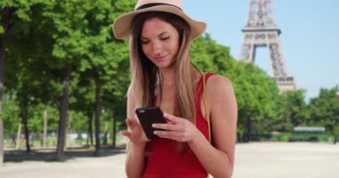 Eiffel Kulesi 'nin telefon uygulamasını kullanan şapka ve kolsuz tişörtlü mutlu bir milenyum kadını. 20 'li yaşlarda hippi bir kız Paris, Fransa' da seyahat ederken akıllı telefondan mesaj atıyor. 4k