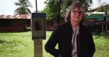 Kosta Rika 'da telefonun yanındaki kameraya bakan son sınıf öğrencisi kadın. Kosta Rika 'da ankesörlü telefonda saçları rüzgarda uçuşan ciddi bir beyaz kadın. 4k