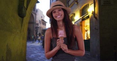 Florence Caddesi 'nde dondurma külahıyla kameraya gülümseyen mutlu bir turist kadın. İtalya 'da tatil yapan beyaz bir kız çilekli dondurmanın tadını çıkarıyor. 4k