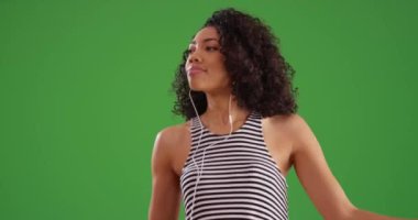 Müzik uygulamasını yeşil ekran arka planında dinleyerek dans eden siyahi kadın. Afrika kökenli Amerikalı kadın milenyum şarkıları cep telefonunda yeşil ekranda. 4k