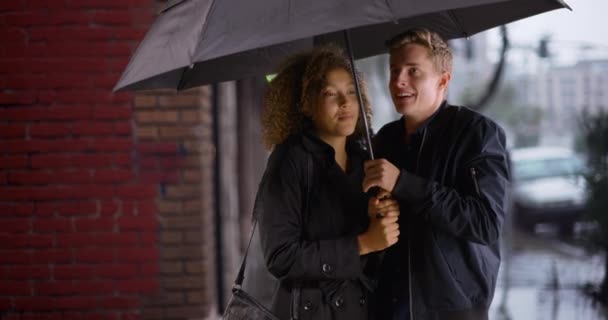 雨が降っている間に傘を持って幸せなスタイリッシュな若い多民族カップル — ストック動画