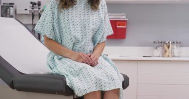 Klinik sandalyesinde oturan ve hastane önlüğü giyen genç bir kadının portresi. Hastane kliniğinde tıbbi koltukta oturan çok ırklı kadına yakından bakın.