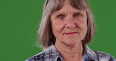 Ciddi bir bilge kadının yeşil krom arka planda kameraya baktığı yakın plan. Yeşil ekranda izole edilmiş kasvetli yaşlı kadının yakın görüntüsü. 4k