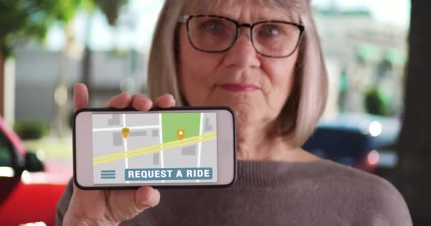 歩道の外に白い高齢者の女性は ライドシェアアプリを開いて携帯電話を保持 ライドシェアアプリでスマートフォンの画面を表示するカジュアルな現代的な老婦人が開きます — ストック動画