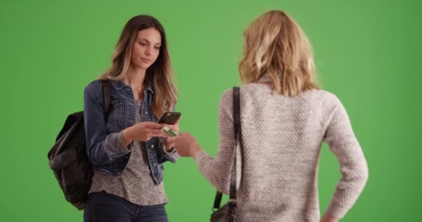 Ładna Blondynka Pokazująca Dziewczynie Zdjęcia Smartfonów Przed Zieloną Ścianą Dwie — Wideo stockowe