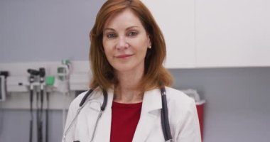 Klinikteki kameraya gülümseyen çekici kıdemli tıp doktorunun yakın çekimi. İçeride olumlu davranışları olan sevimli orta yaşlı bir doktorun portresi.