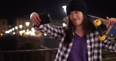 Milenyum patencisi akıllı telefon kamerasıyla selfie çekiyor ve Floransa 'da Arno nehrinde kaykay tutuyor. Avrupa 'da fotoğraf çekmek için teknolojiyi kullanan genç Asyalı kadın portresi. 4k