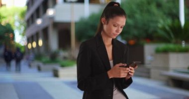 Milenyum iş kadını ofis parkında akıllı telefondan mesaj atıyor. 4G mobil cihaz kullanan başarılı bir kadın spor ceket giyiyor. 4k