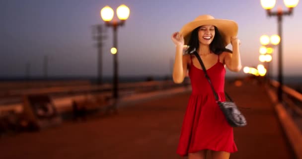 年轻的白人女孩穿着红色的太阳衣和软帽在码头上跳舞 千年白人妇女日落时在码头上玩得很开心 — 图库视频影像
