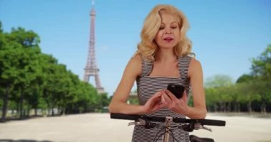 Bisikletli güzel bir kadın yol tarifi için cep telefonunda uygulama kullanıyor. Paris, Fransa 'da bisiklet süren kadın turist akıllı telefondan harita kullanıyor. 4k