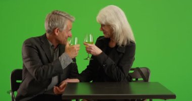 Arka planda bulanık bir şekilde oturan mutlu çift yeşil ekranda şampanya içiyor. Anahtar ya da birleşik olmak üzere yeşil ekranda.