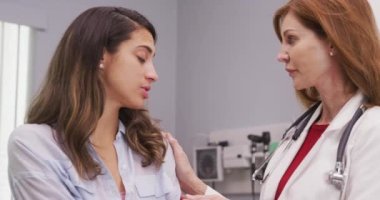 Güzel Latin kadın, omuz yaralanması hakkında kıdemli doktorla görüşüyor. Orta yaşlı doktorun genç kadın hastayı sağlık durumuyla ilgili teselli etmesine yakından bakın.