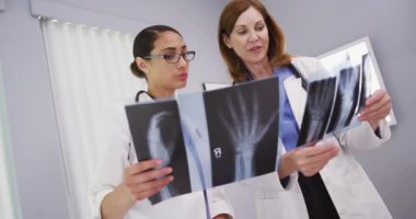 Güzel Latin doktorların, kıdemli meslektaşlarıyla hasta röntgenleri hakkında konuştuklarını yakın plan. Hastanedeki el ve bilek röntgenlerini inceleyen iki tıp doktorunun portresi.