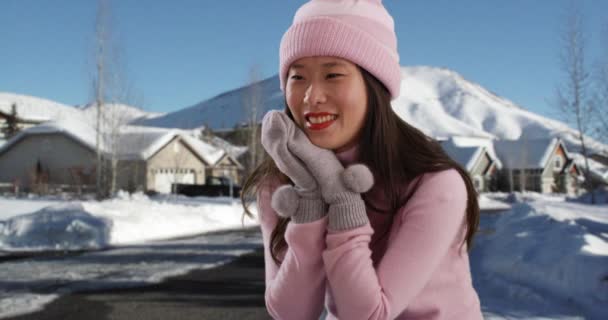 在多雪的郊区城镇里 快乐的千禧年女人端坐着 穿着冬装 在雪地铺天盖地的街道上 可以近距离看到可爱的年轻亚洲女性戴着便帽和手套 — 图库视频影像