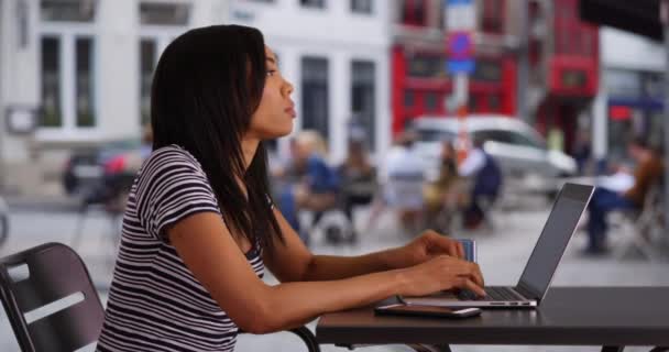 仕事の電子メールに答える彼女のラップトップで街の通りの黒人女性の側面図 コーヒーをコンピューターに入力して屋外に座っているビジネス女性 — ストック動画