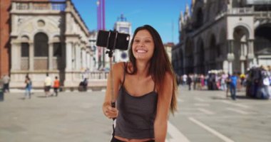 İtalya 'da tatil yapan sevimli bir milenyum kızı St. Mark Meydanı' nda selfie çekiyor. Venedik 'te selfie çubuğu kullanan turist kadın, surat yapıp işaret ediyor. 4k