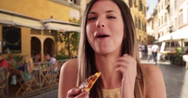 İtalya 'da seyahat ederken gülen ve pizza yiyen bin yıllık bir kızın yakın çekimi. İtalyan restoranının önünde pizza yemekten hoşlanan çekici bir kadın. 4k