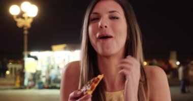 Bin yıllık kızın benzin istasyonundan aldığı pizzaları yiyip gülüşünün yakın çekimi. Kahverengi saçlı çekici bir kadın benzin istasyonunda pizza yiyor. 4k