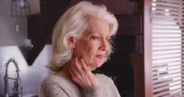 Depresyondaki yaşlı kadının elini boynuna dayadığı yakın plan. Mutfak içinde iç çeken üzgün, düşünceli, beyaz bir kadın. 4k